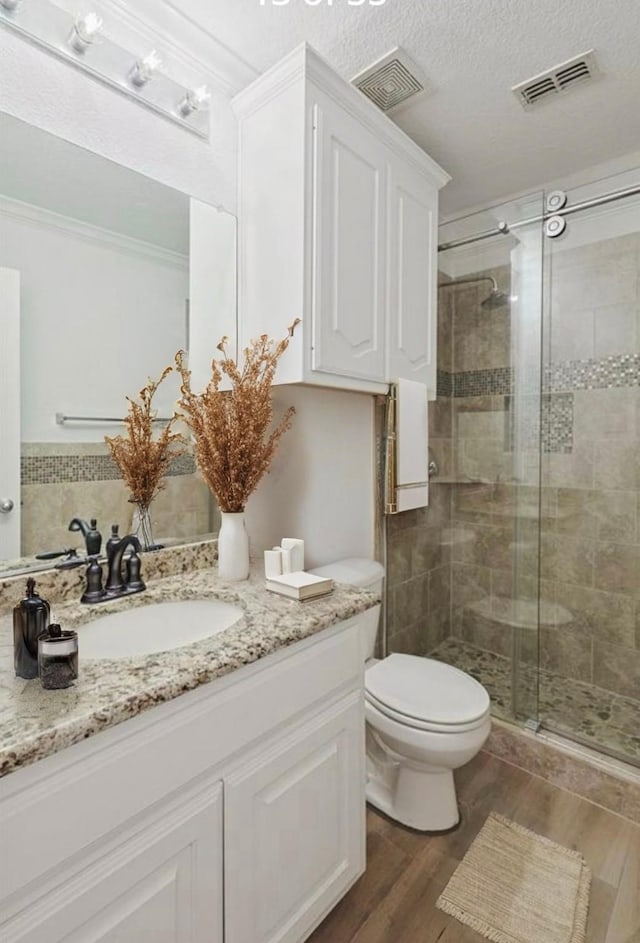 bathroom with a shower with shower door, wood-type flooring, vanity, toilet, and a textured ceiling