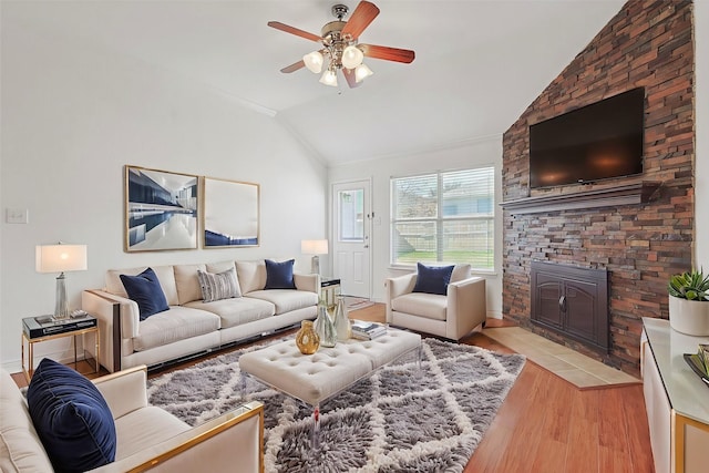 living room featuring vaulted ceiling, a stone fireplace, ceiling fan, light hardwood / wood-style floors, and crown molding