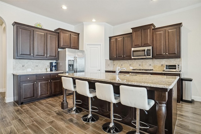 kitchen featuring dark hardwood / wood-style floors, an island with sink, a kitchen breakfast bar, dark brown cabinetry, and stainless steel appliances