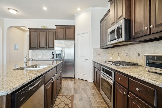 kitchen with sink, crown molding, stainless steel appliances, dark brown cabinetry, and light hardwood / wood-style floors