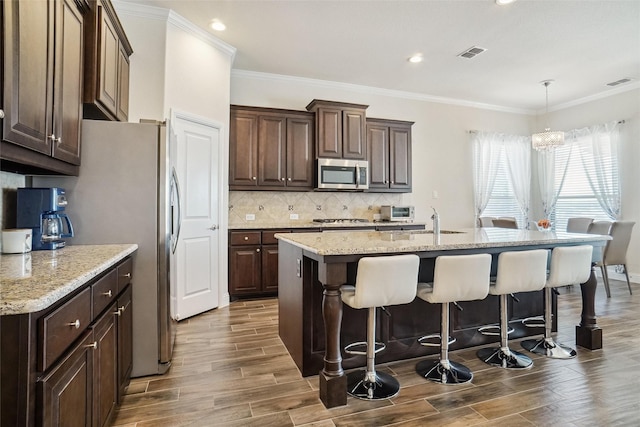 kitchen with a kitchen island with sink, light stone countertops, decorative light fixtures, and stainless steel appliances