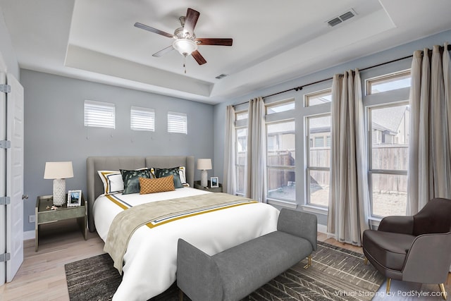 bedroom featuring a raised ceiling, multiple windows, and light hardwood / wood-style flooring