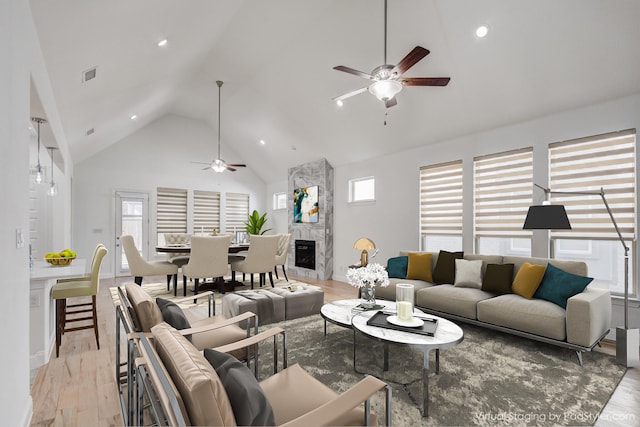 living room with ceiling fan, a high end fireplace, high vaulted ceiling, and light wood-type flooring