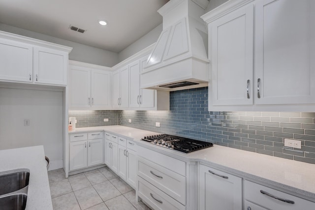 kitchen with custom exhaust hood, light tile patterned floors, white cabinets, stainless steel gas stovetop, and backsplash