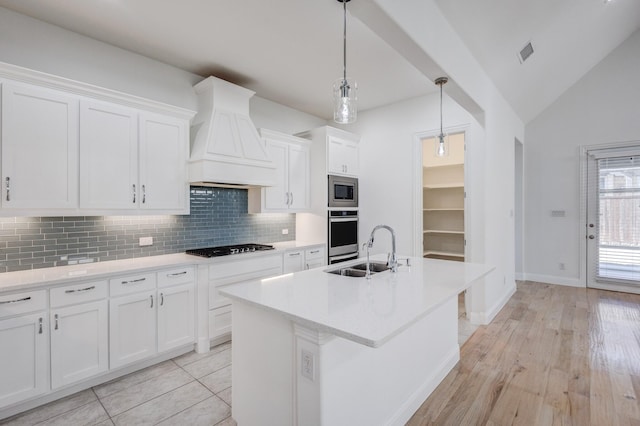 kitchen featuring sink, premium range hood, stainless steel appliances, an island with sink, and white cabinets