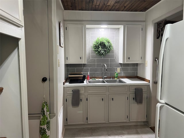 kitchen featuring light countertops, backsplash, freestanding refrigerator, and a sink