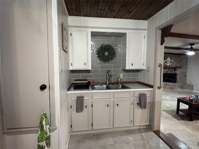 kitchen with a ceiling fan, a fireplace, a sink, light countertops, and white cabinetry