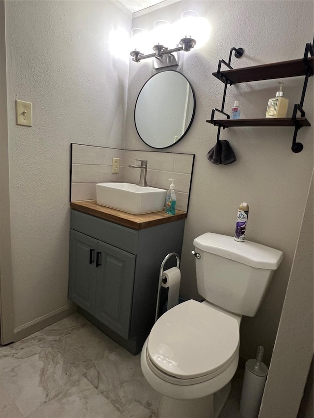 bathroom with marble finish floor, toilet, vanity, and a textured wall