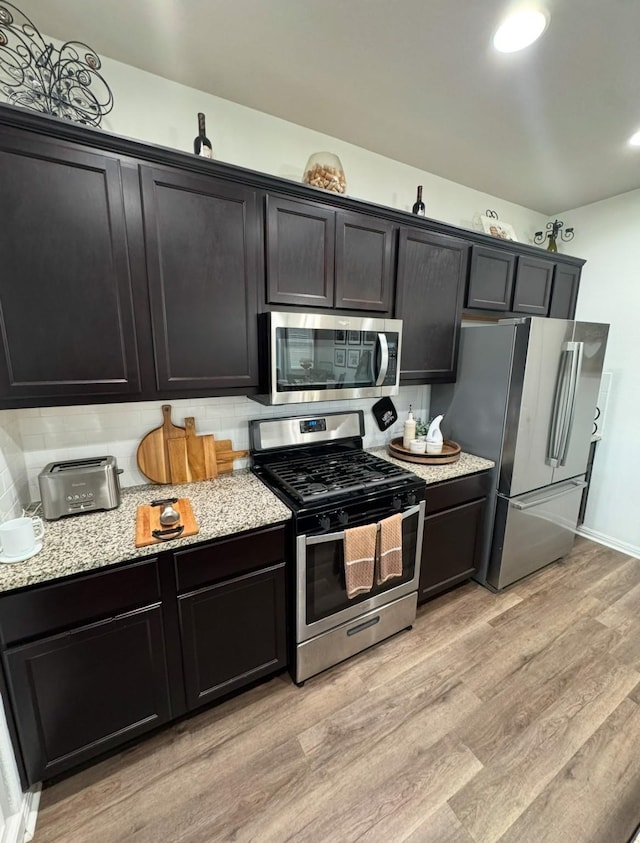 kitchen with tasteful backsplash, stainless steel appliances, light stone countertops, and light hardwood / wood-style flooring