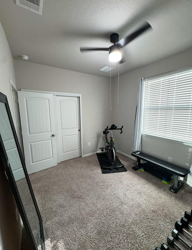 workout area featuring ceiling fan, carpet, and a textured ceiling