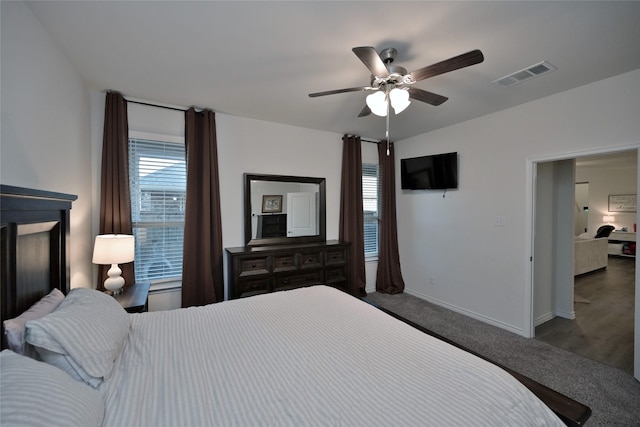 bedroom with ceiling fan, dark carpet, and multiple windows