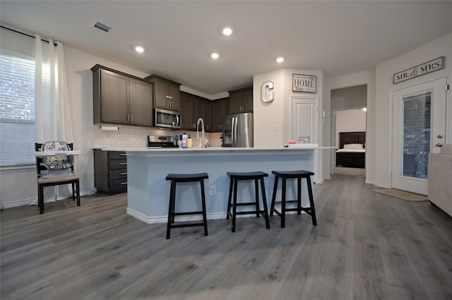 kitchen featuring a kitchen bar, dark brown cabinets, a center island with sink, appliances with stainless steel finishes, and hardwood / wood-style flooring