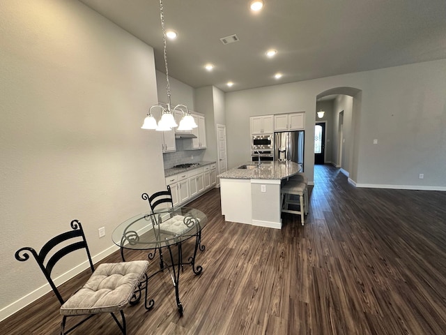 kitchen featuring hanging light fixtures, stainless steel appliances, dark hardwood / wood-style floors, light stone counters, and a center island with sink