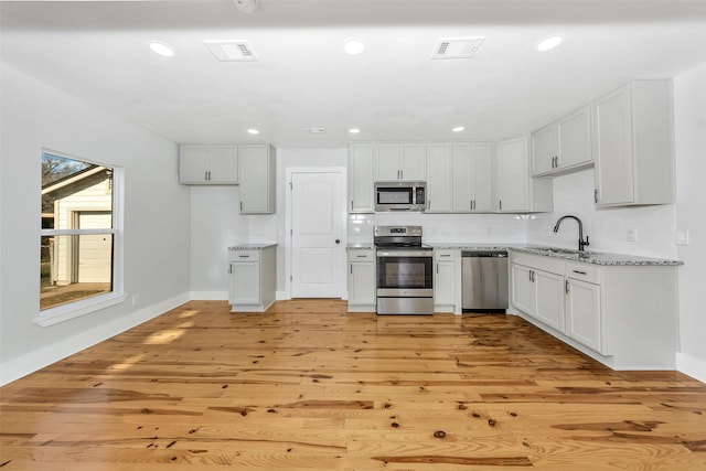 kitchen with sink, light hardwood / wood-style flooring, appliances with stainless steel finishes, white cabinets, and decorative backsplash