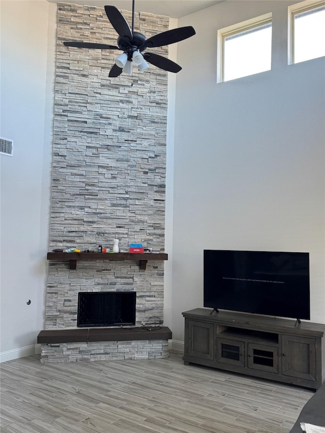 living room with a stone fireplace, light wood-type flooring, and ceiling fan