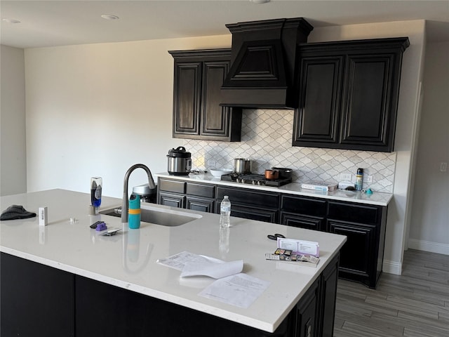 kitchen with an island with sink, sink, backsplash, and custom range hood