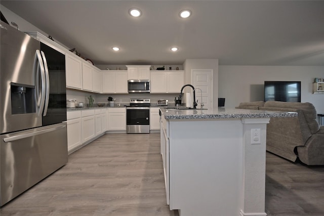 kitchen featuring light stone counters, stainless steel appliances, an island with sink, and white cabinets