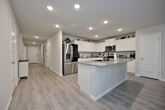 kitchen with appliances with stainless steel finishes, white cabinets, light stone countertops, a center island with sink, and light hardwood / wood-style flooring