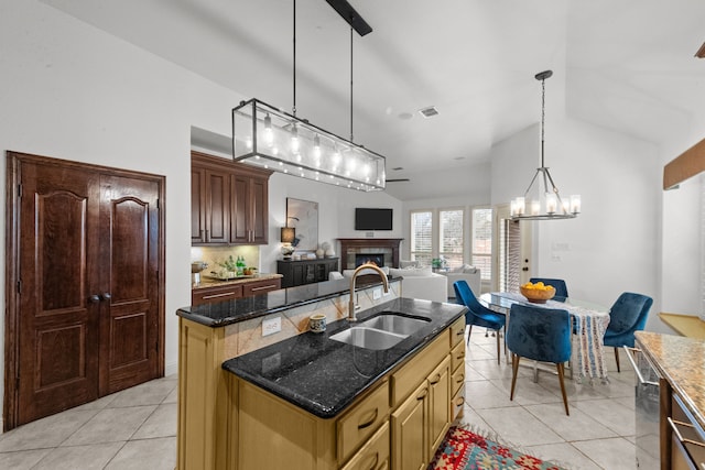 kitchen featuring pendant lighting, sink, light tile patterned floors, a kitchen island with sink, and dark stone counters