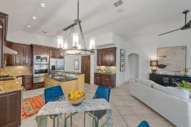 kitchen with lofted ceiling, sink, tasteful backsplash, stainless steel appliances, and a kitchen island with sink