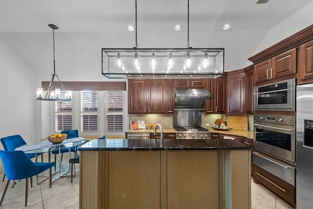 kitchen with pendant lighting, dark stone counters, a kitchen island with sink, and tasteful backsplash