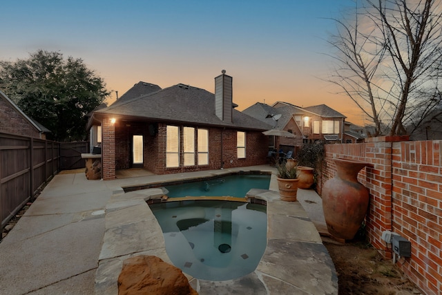 back house at dusk with a swimming pool with hot tub and a patio area