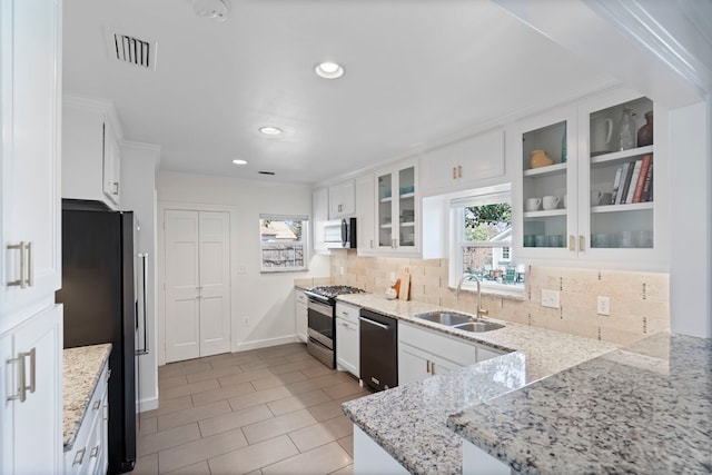 kitchen featuring sink, appliances with stainless steel finishes, white cabinetry, backsplash, and light stone countertops