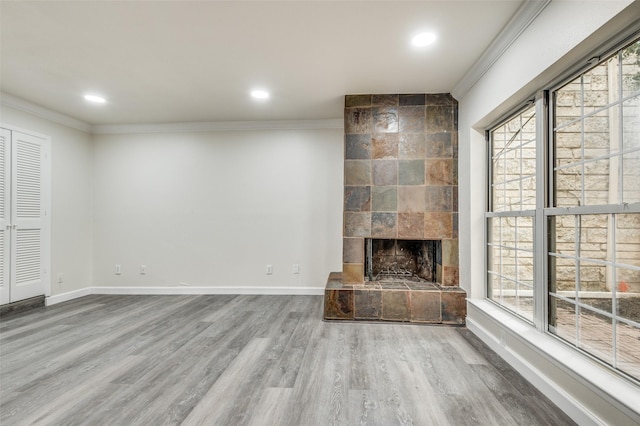 unfurnished living room featuring a healthy amount of sunlight, ornamental molding, a tiled fireplace, and hardwood / wood-style floors