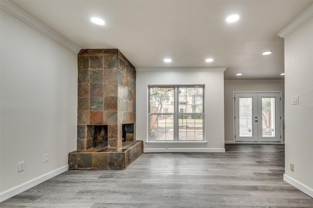 unfurnished living room featuring a tiled fireplace, wood-type flooring, ornamental molding, and french doors