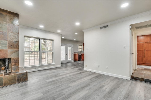 unfurnished living room with a tiled fireplace, crown molding, wood-type flooring, and plenty of natural light