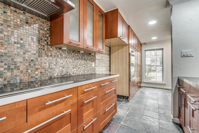 kitchen with tasteful backsplash, stovetop, wall chimney range hood, and oven