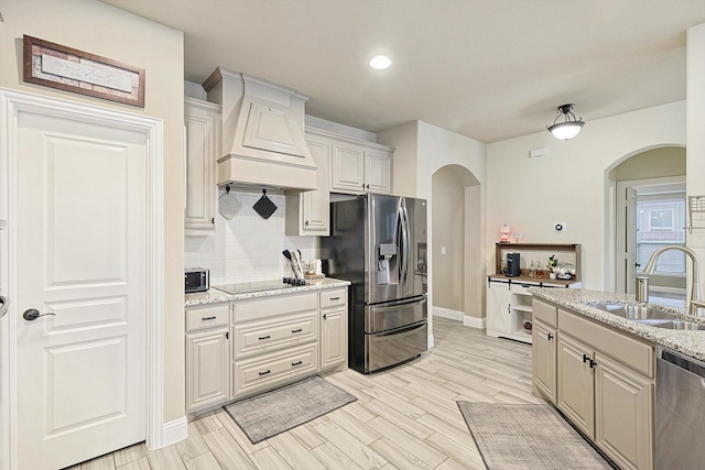 kitchen featuring premium range hood, sink, decorative backsplash, stainless steel appliances, and light stone countertops