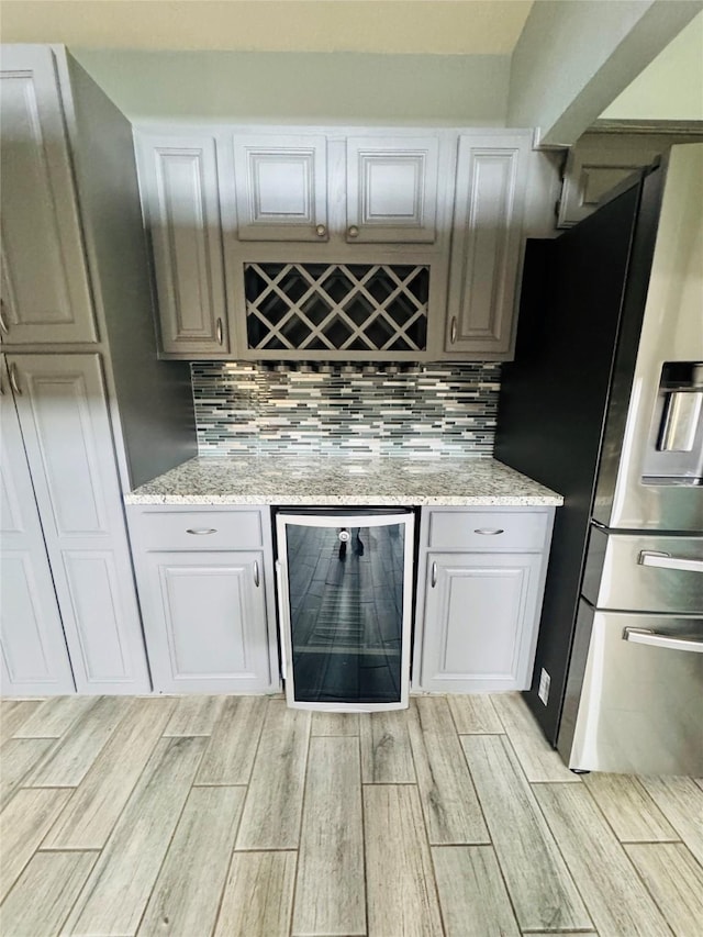 bar featuring tasteful backsplash, white cabinetry, stainless steel fridge, wine cooler, and light stone counters