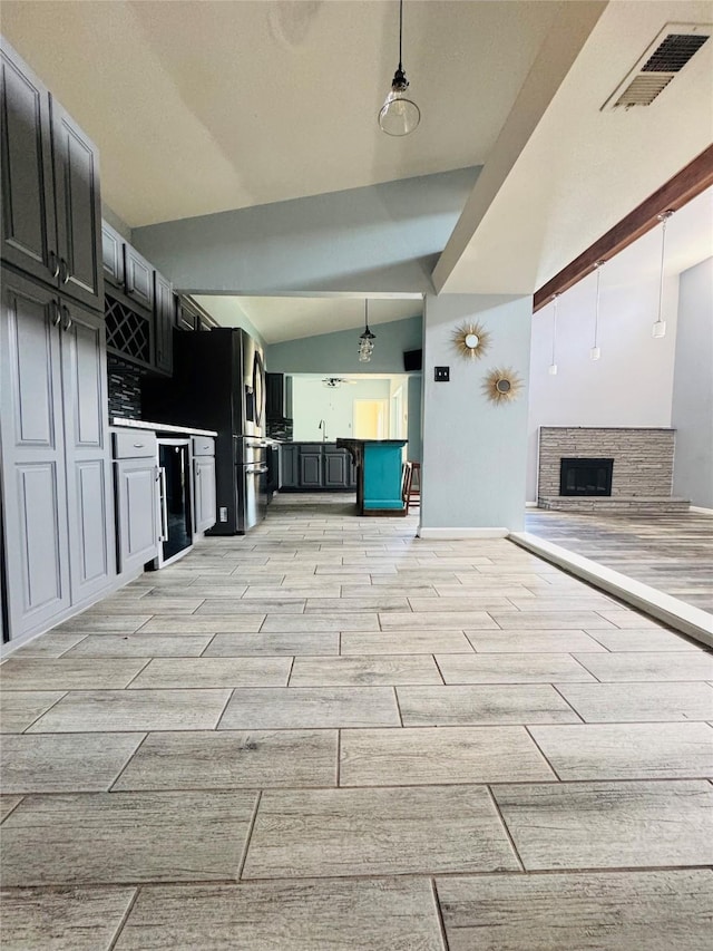 kitchen with vaulted ceiling, a stone fireplace, and pendant lighting