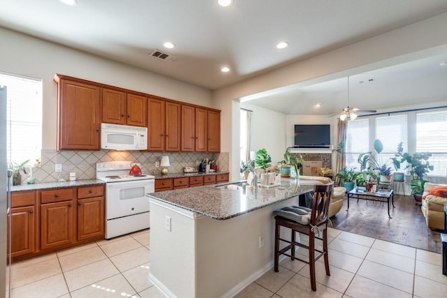 kitchen featuring an island with sink, a kitchen bar, light tile patterned floors, light stone countertops, and white appliances