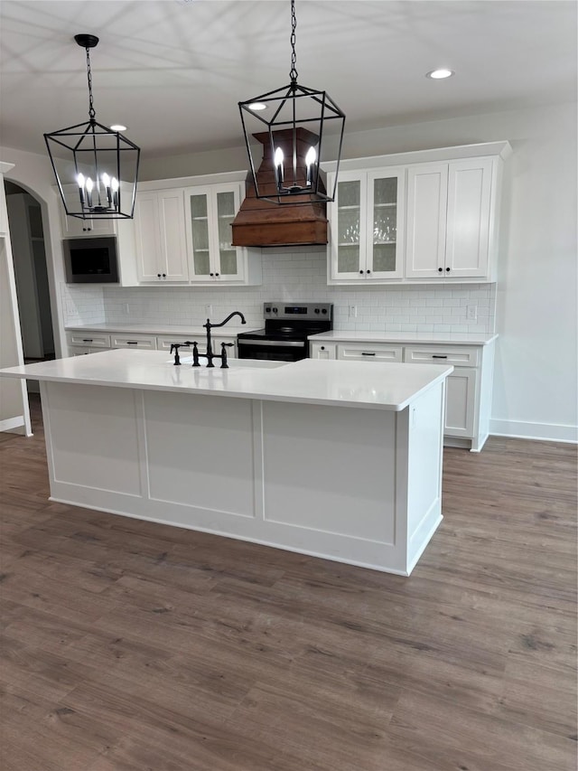 kitchen with dark wood-type flooring, electric range, an island with sink, decorative backsplash, and white cabinets