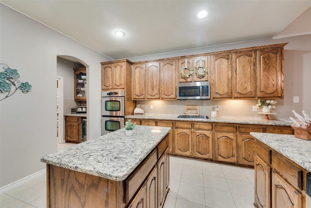 kitchen featuring tasteful backsplash, light tile patterned floors, appliances with stainless steel finishes, a kitchen island, and light stone countertops