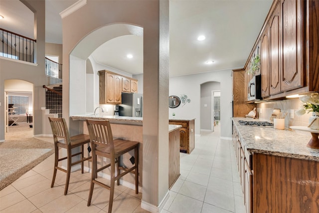 kitchen featuring light tile patterned floors, a breakfast bar area, appliances with stainless steel finishes, backsplash, and light stone counters