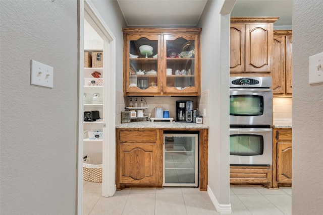 bar featuring light tile patterned floors, beverage cooler, double oven, and decorative backsplash