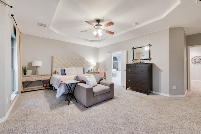 bedroom featuring ceiling fan, ensuite bath, a raised ceiling, and light carpet