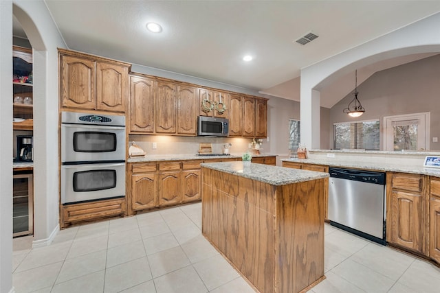 kitchen featuring stainless steel appliances, a kitchen island, hanging light fixtures, and light stone counters