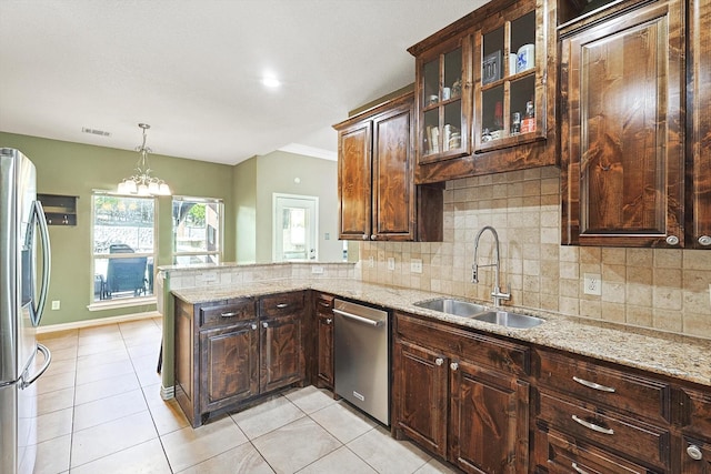 kitchen featuring light stone counters, stainless steel appliances, hanging light fixtures, dark brown cabinetry, and a sink