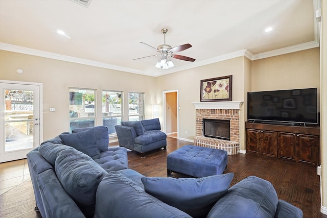 living area with ornamental molding, dark wood-style flooring, a brick fireplace, and a ceiling fan