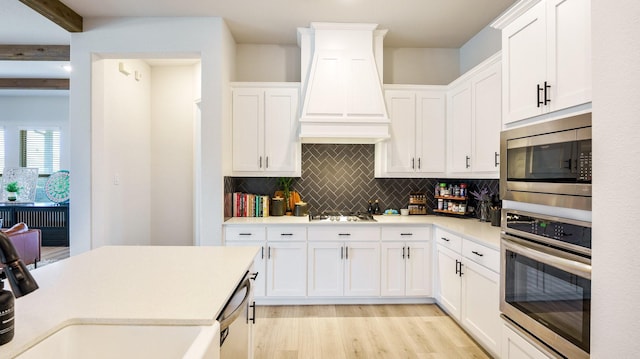 kitchen with white cabinetry, backsplash, custom range hood, and appliances with stainless steel finishes