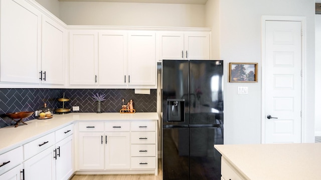 kitchen featuring white cabinetry, decorative backsplash, and black fridge