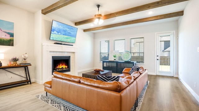 living room featuring beamed ceiling, ceiling fan, a fireplace, and light hardwood / wood-style floors