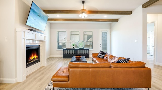 living room with a tiled fireplace, ceiling fan, light hardwood / wood-style floors, and beam ceiling