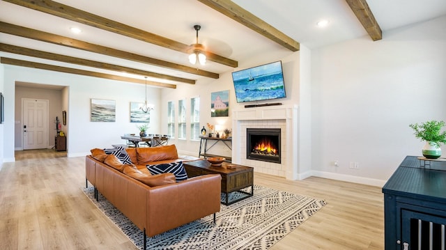 living room featuring beam ceiling, ceiling fan with notable chandelier, a fireplace, and light hardwood / wood-style floors