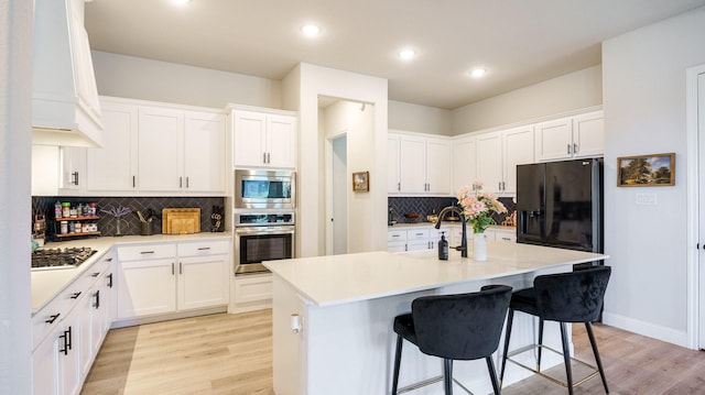 kitchen featuring a kitchen bar, a center island with sink, white cabinets, and appliances with stainless steel finishes