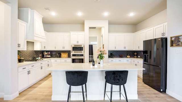 kitchen with a kitchen bar, white cabinetry, a center island, appliances with stainless steel finishes, and custom range hood